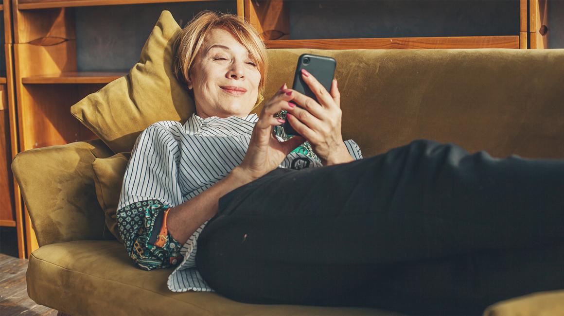 Ruda 50latka na kanapie z telefonem