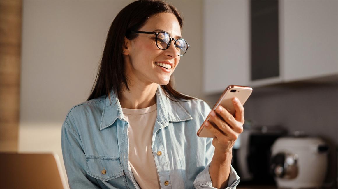 W kuchni kobieta z uśmiechem patrzy na komórkę