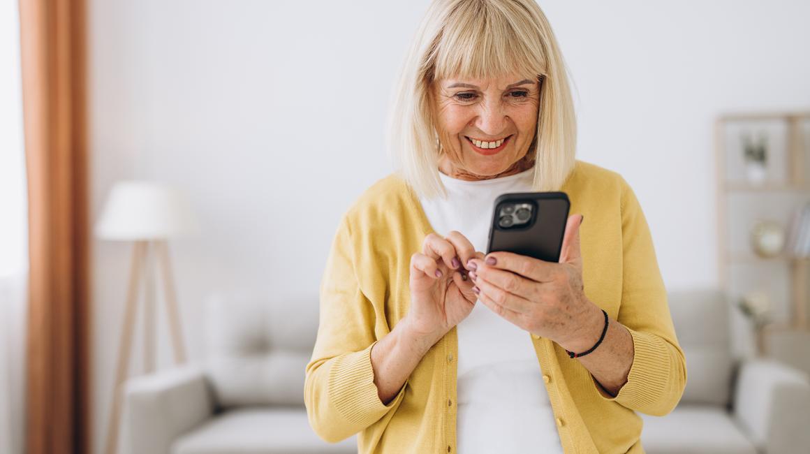 Seniorka z komorka w domu, w rozpiętym swetrze