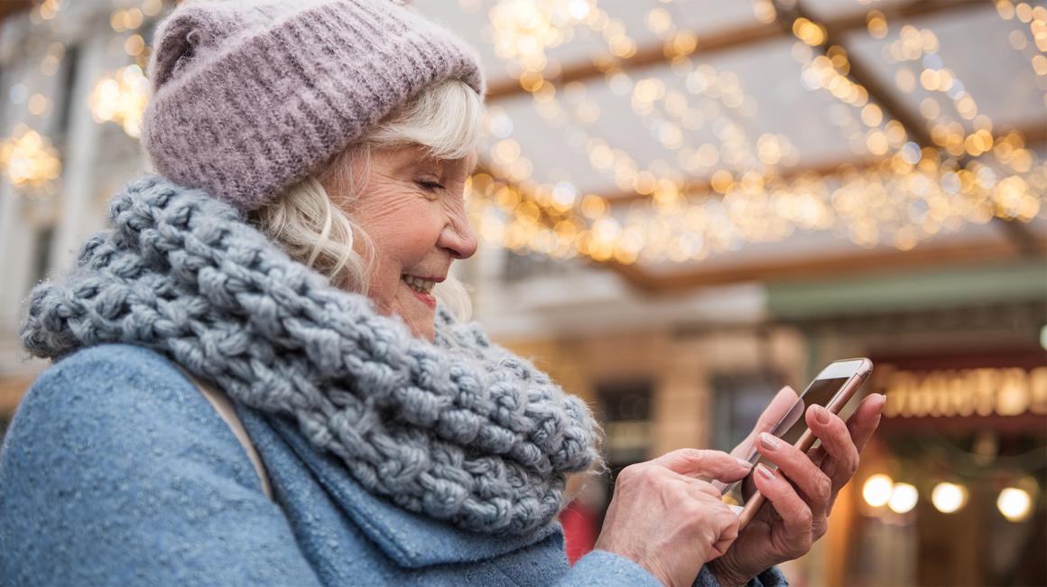 starsza pani w cieplej czapce na dworze, z komórką w reku