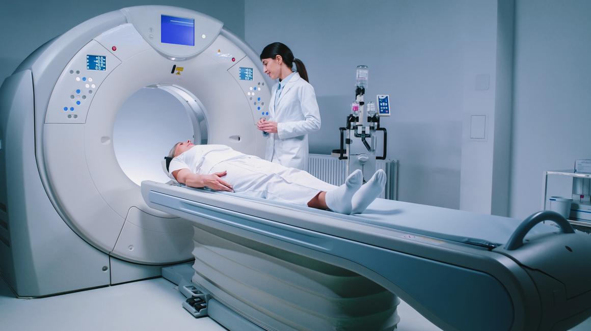 osoba leży na łóżku tomografu, obok stoi pielęgniarka