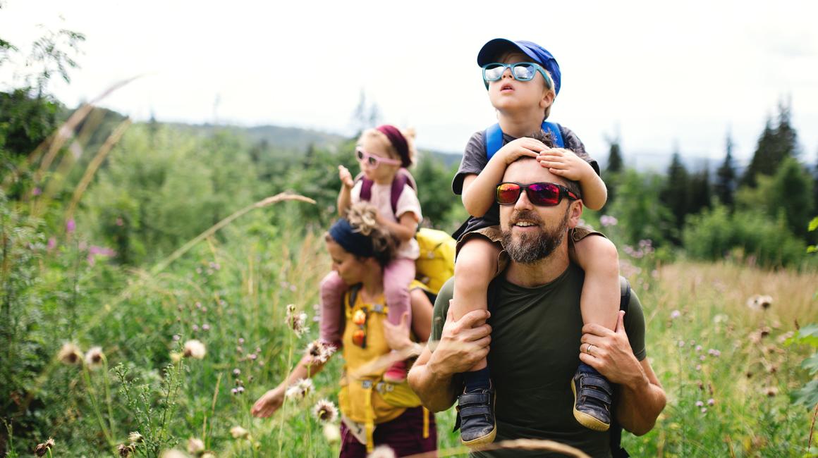 łąka z wysoką trawą, rodzice niosą dzieci na barana