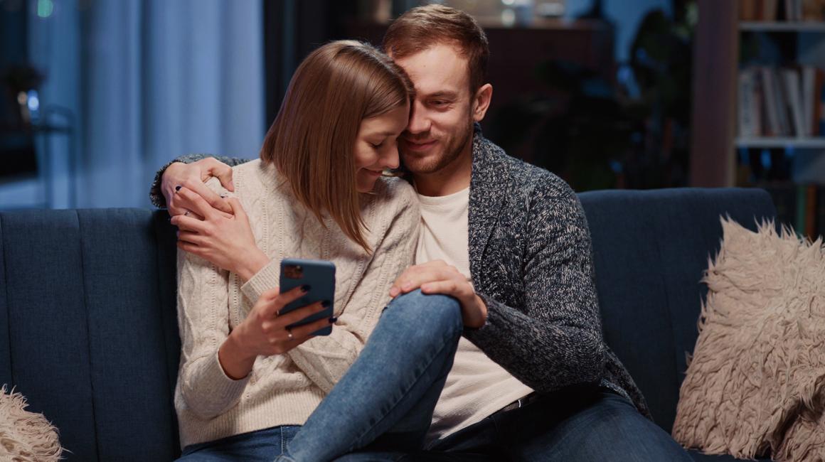 Przytulona para na kanapie, ona trzyma w ręku komórkę
