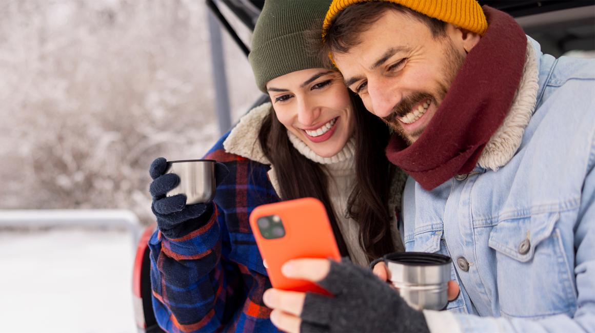 Usmiechnieta para patrzy na telefon, w tle zimowy krajobraz