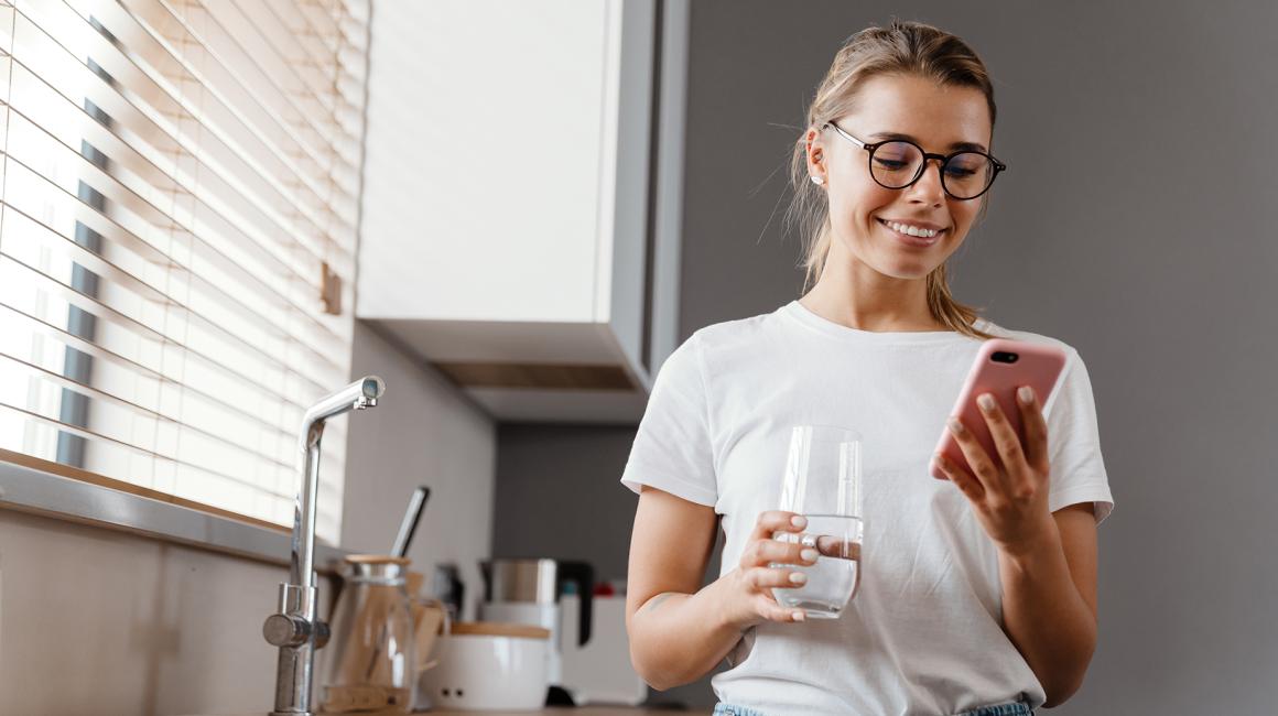 Dziewczyna w białym t-shircie ze szklanką wody i komórką w kuchni