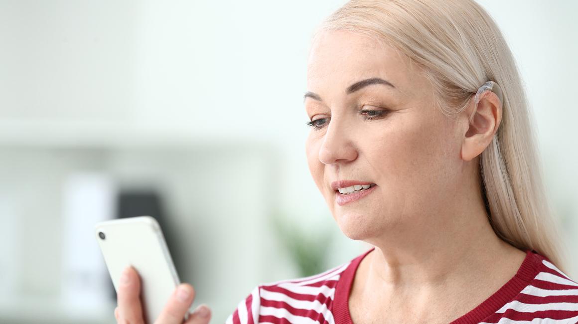 Blondynka z aparatem słuchowym patrzy na telefon 