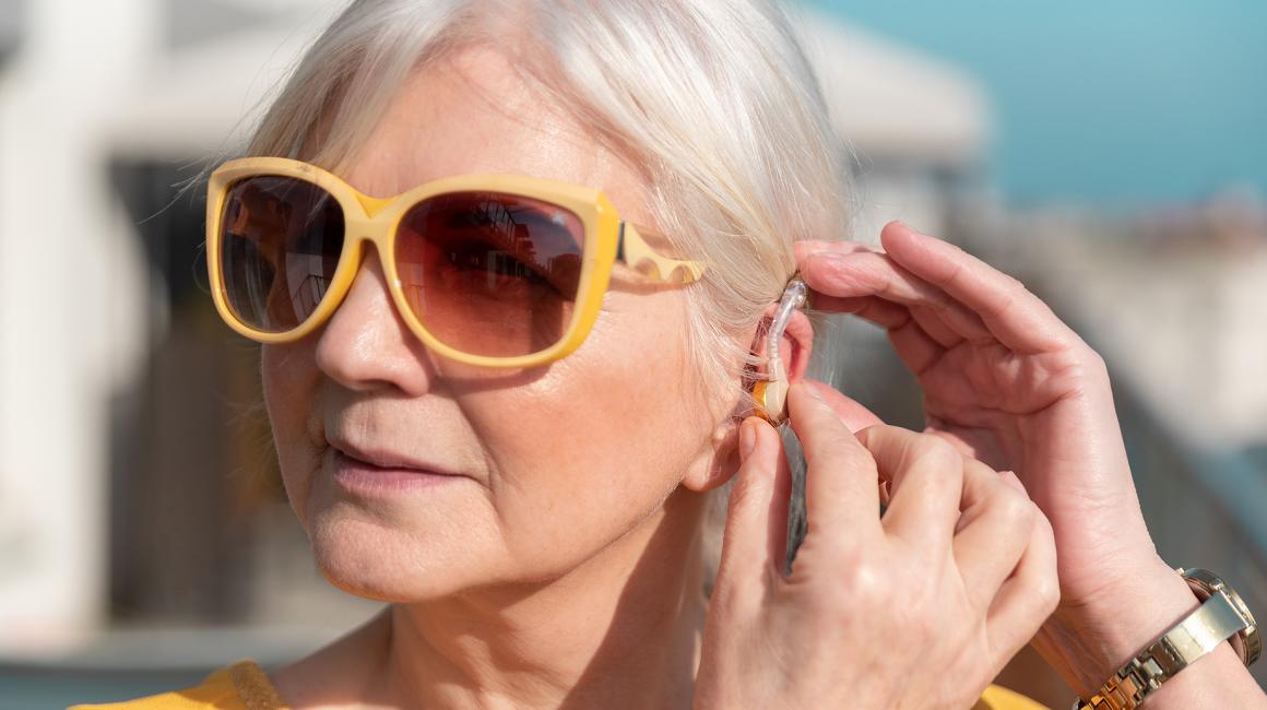 kobieta z aparatem słuchowym, w ciemnych okularach, siwe włosy