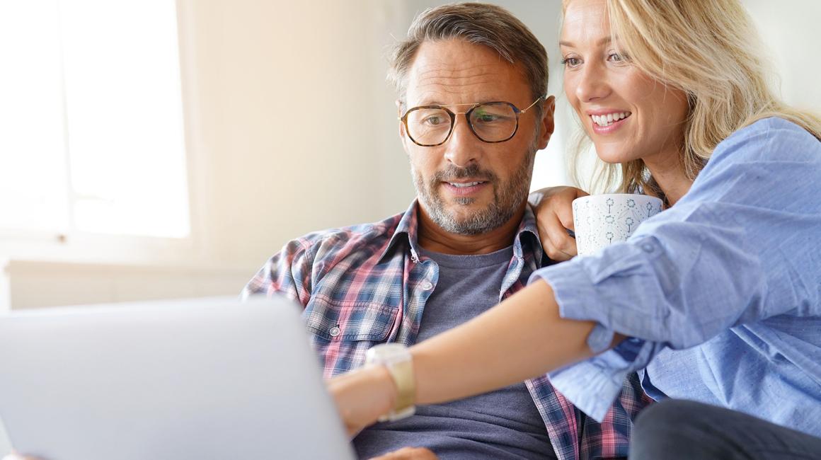 Kobieta z kubkiem kawy pokazuje coś na ekranie kompa mężczyźnie