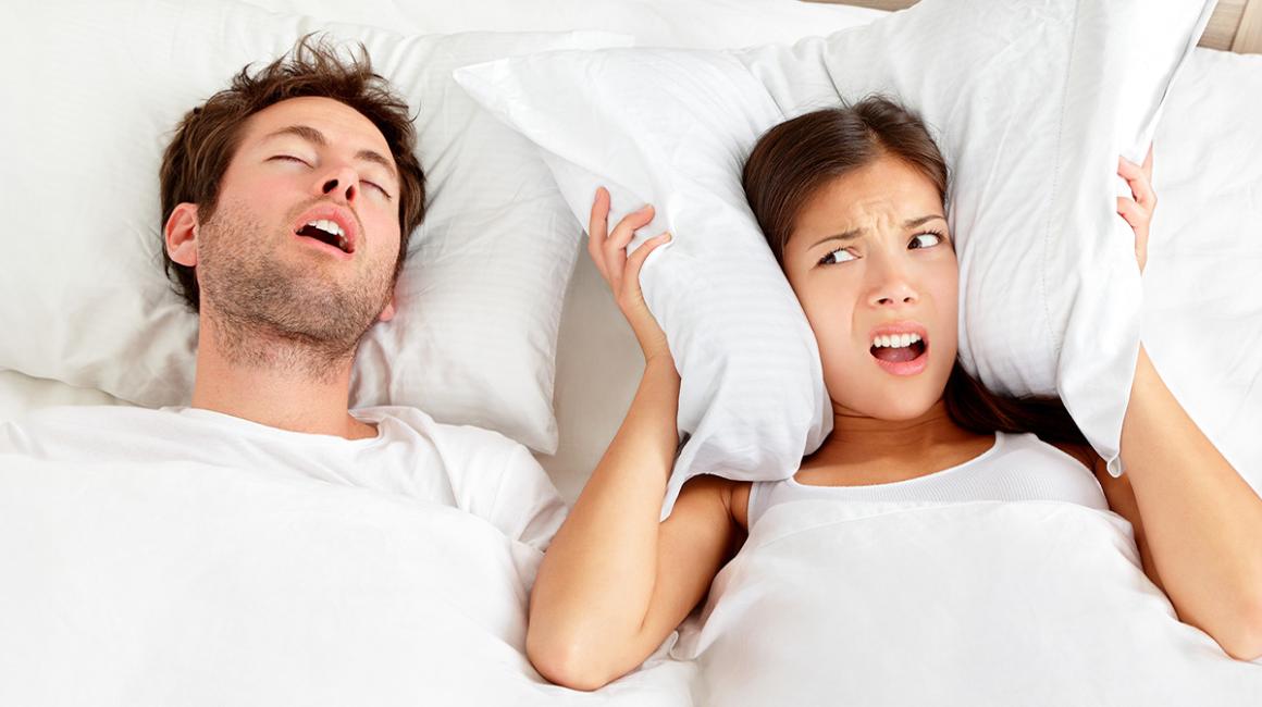 mężczyzna chrapie, obok kobieta poduszką zakrywa uszy