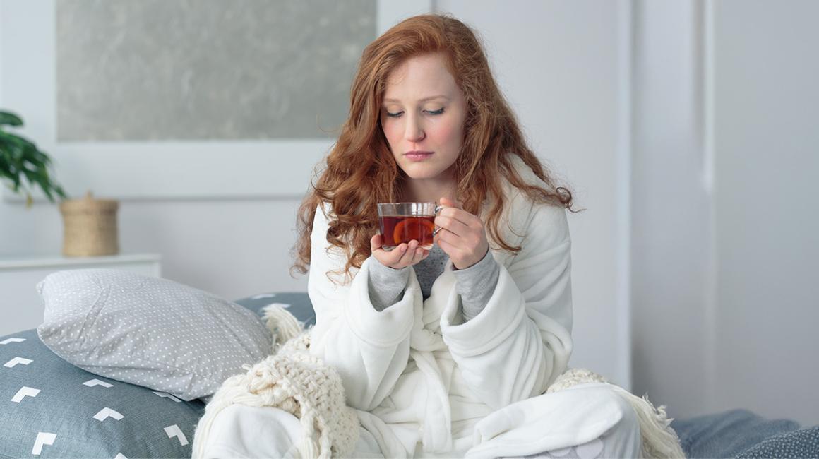 Młoda kobieta siedzi na łóżku z kubkiem herbaty