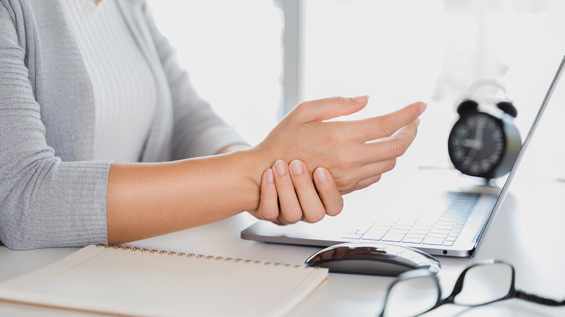 kobieta przy komputerze trzyma się za rękę