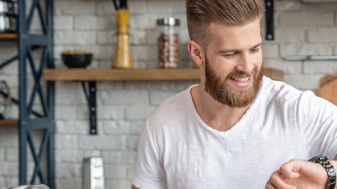 Młody mężczyzna w kuchni patrzy na zegarek 