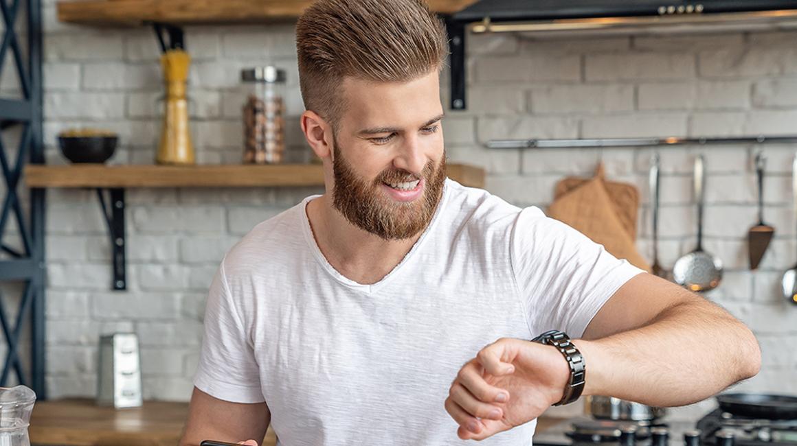 Młody mężczyzna w kuchni patrzy na zegarek