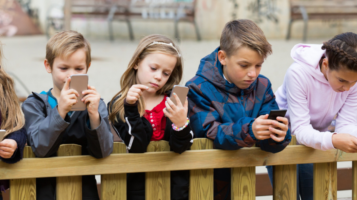 Dzieci dtoją przypłocie i patrzą w telefony