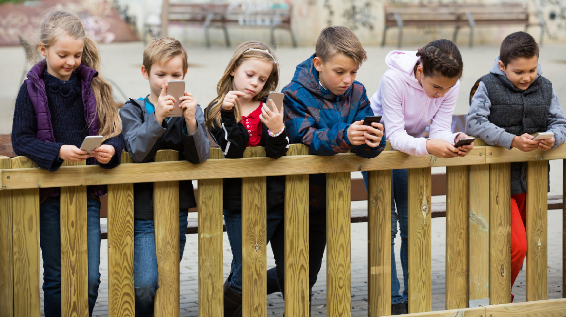 dzieci stoją przy płocie i patrzą w telefony