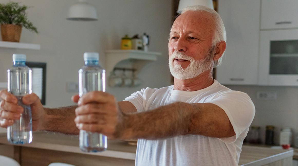 starszy pan ćwiczy w domu z małymi butelkami wody