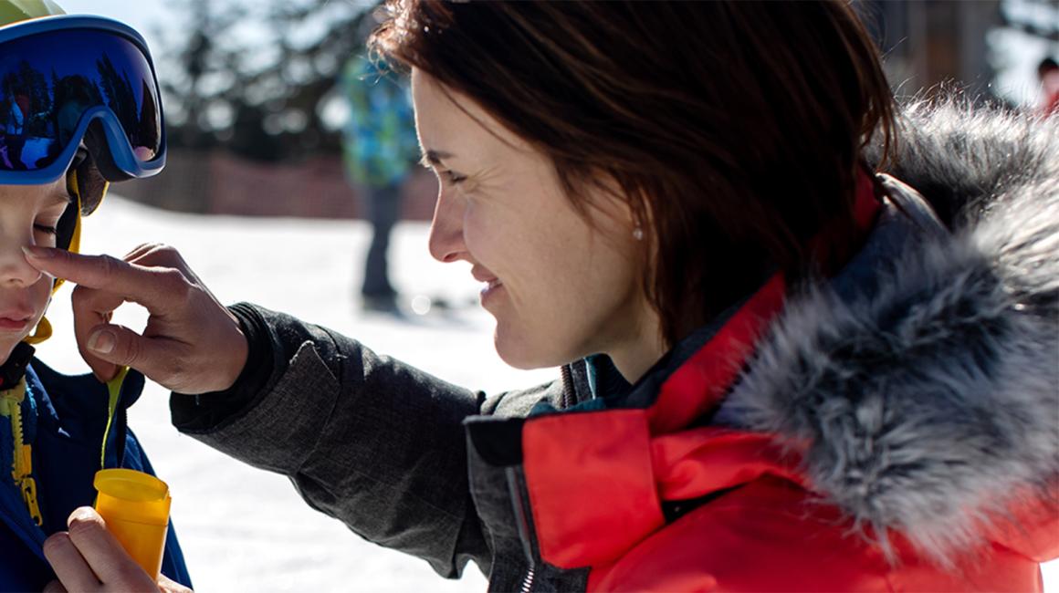 mama smaruje dziecku nos, oboje na stoku narciarskim