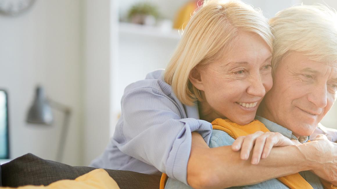 50letnia pani obejmuje za szyję męza, on patrz w laptop
