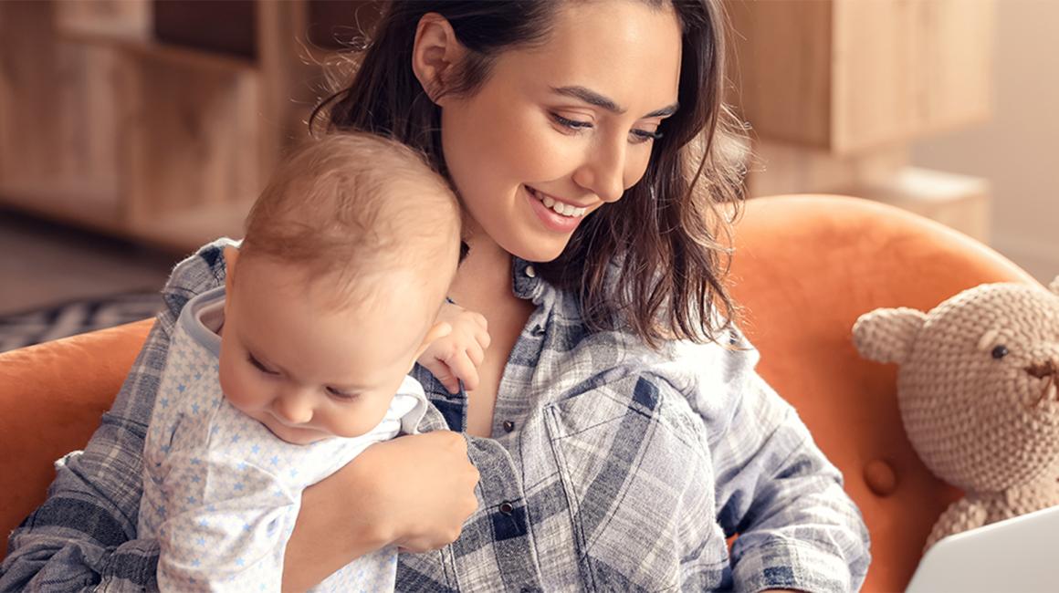 Matka z rocznym dzieckiem na kanapie, laptop ma na kolanach
