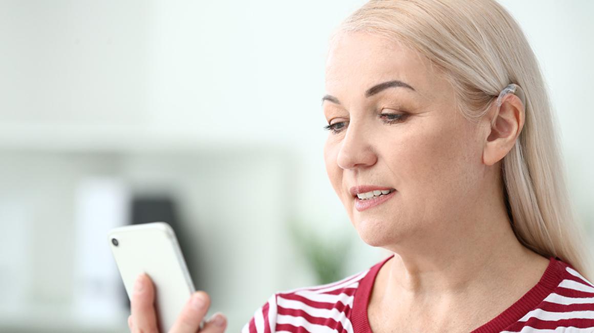 Blondynka z aparatem słuchowym patrzy na telefon 