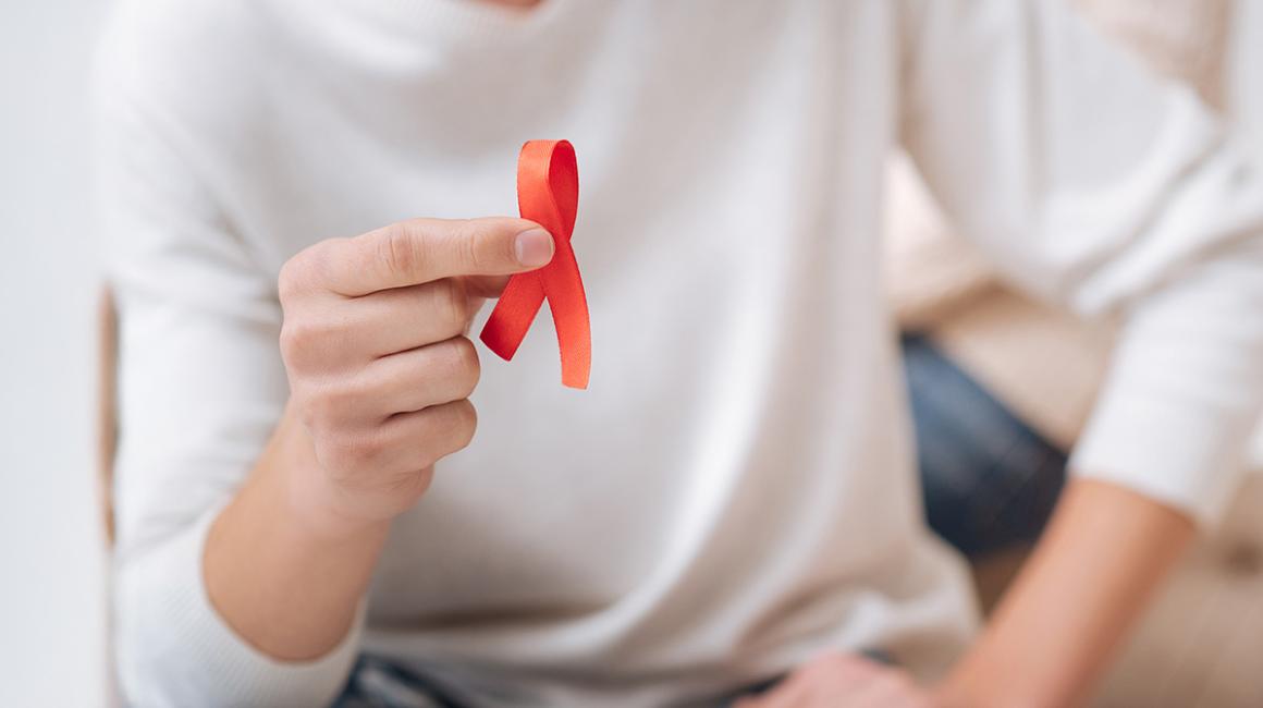 ręka trzymająca czerwoną wstążkę symbol AIDS
