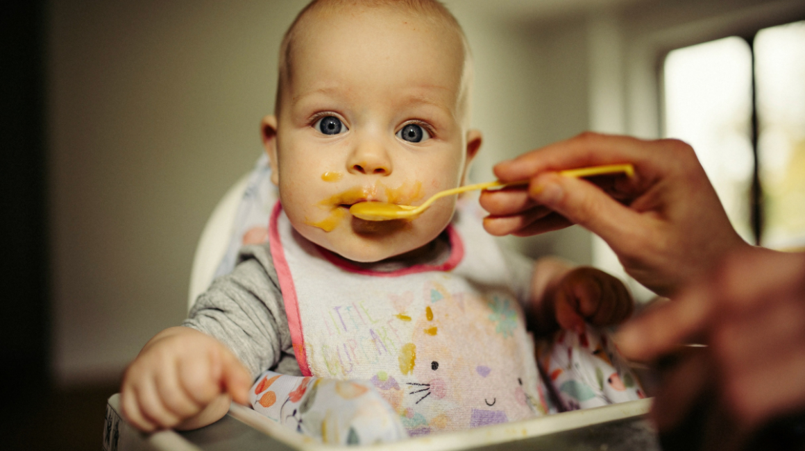 Dziecko siedzi w krzesełku dla dzieci i jest karmione łyżeczką