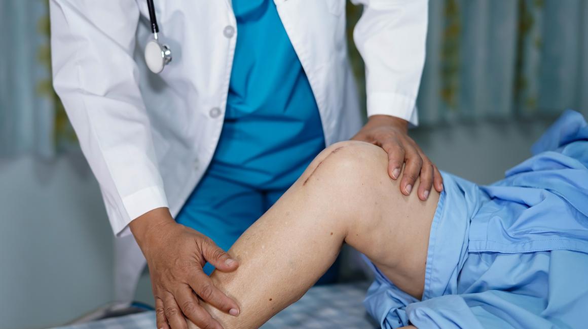 lekarz ogląda kolano pacjenta z blizną