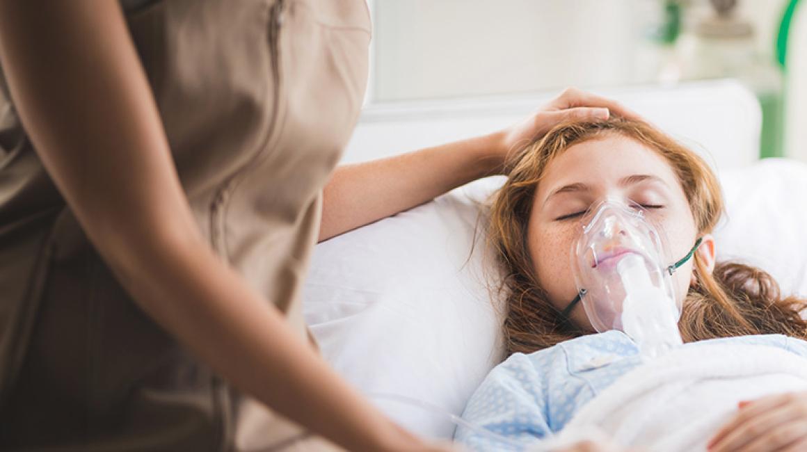 Dziewczynka leży wbłóżku w masce tlenowej