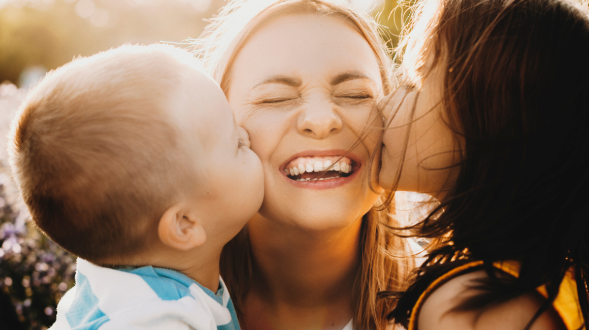 Dwoje dzieci całuje w policzki uśmiechniętą mamę