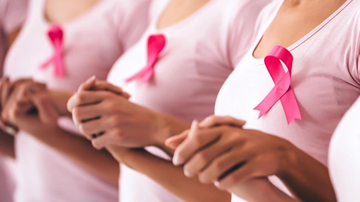 Kobiety w różowych koszulkach z przyczepionymi różowymi wstążkami stoją i trzymają się za ręce.