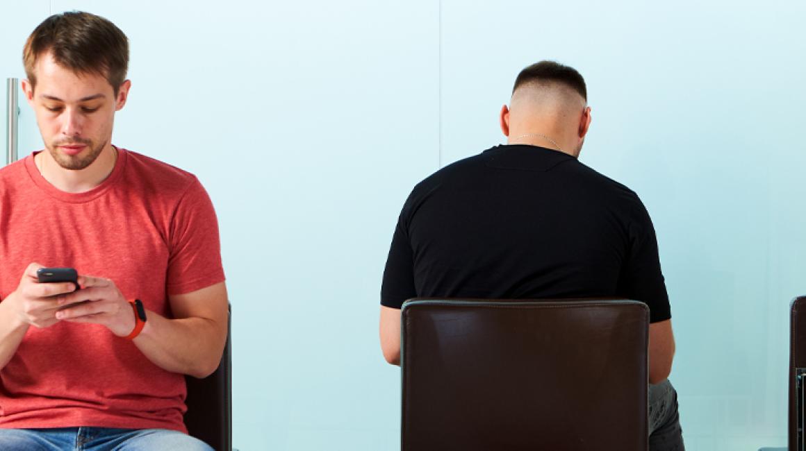 Trzy osoby siedzą na krzesłach w poczekalni w przychodni. Patrzą w telefony.