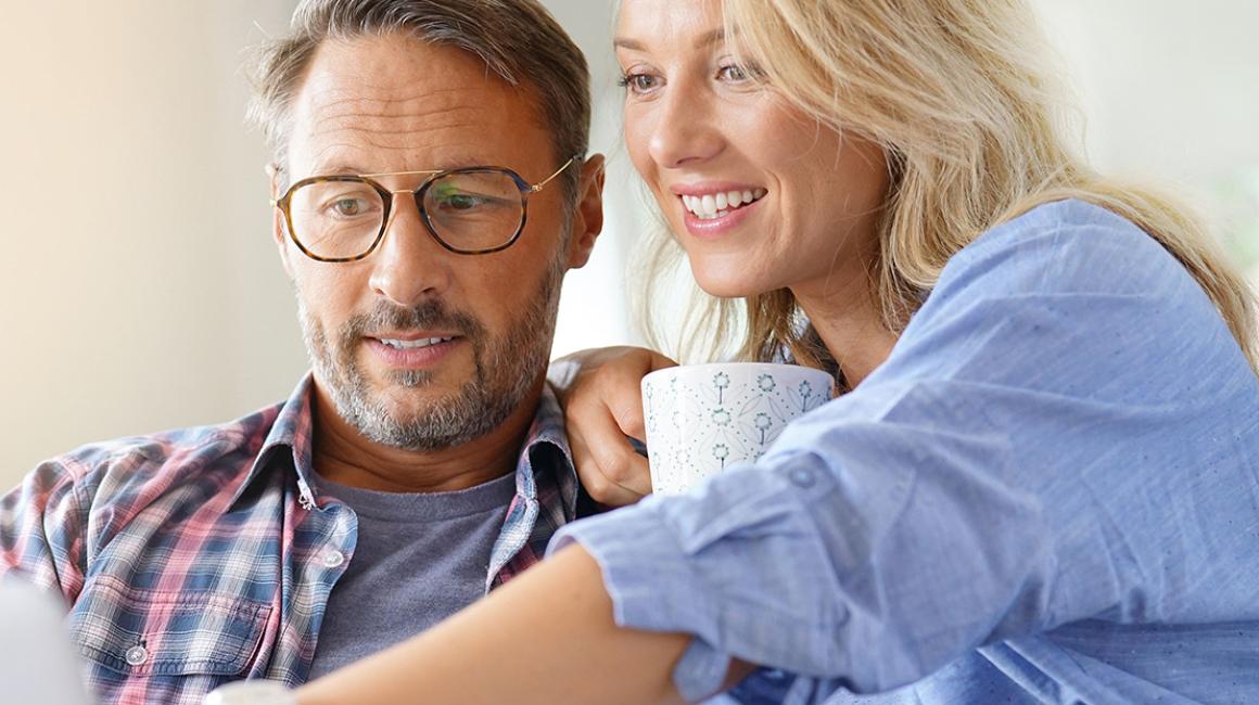 Kobieta z kubkiem kawy pokazuje coś na ekranie kompa mężczyźnie