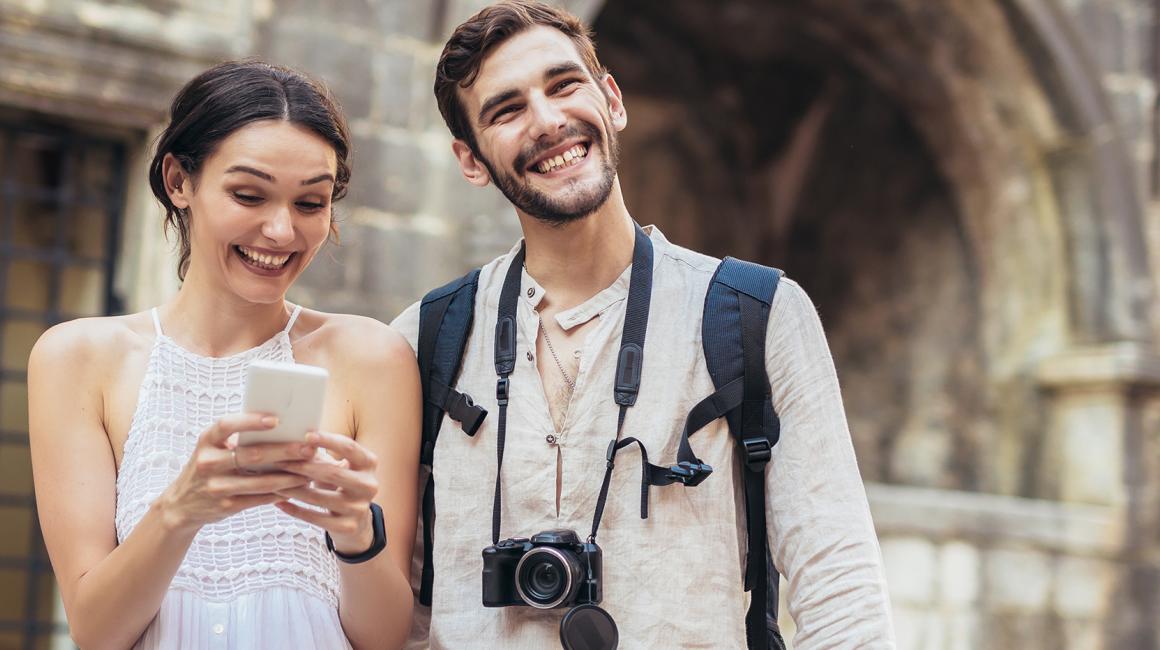 Dziewczyna i chłopak stoją na tle zabytkowej budowli. Dziewczyna robi cioś na telefonie.
