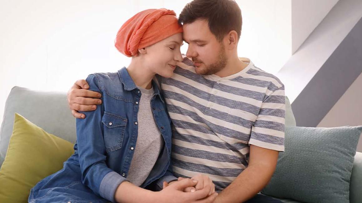 Młody mężczyzna i kobieta z chustką na głowie siedzą przytuleni na kanapie