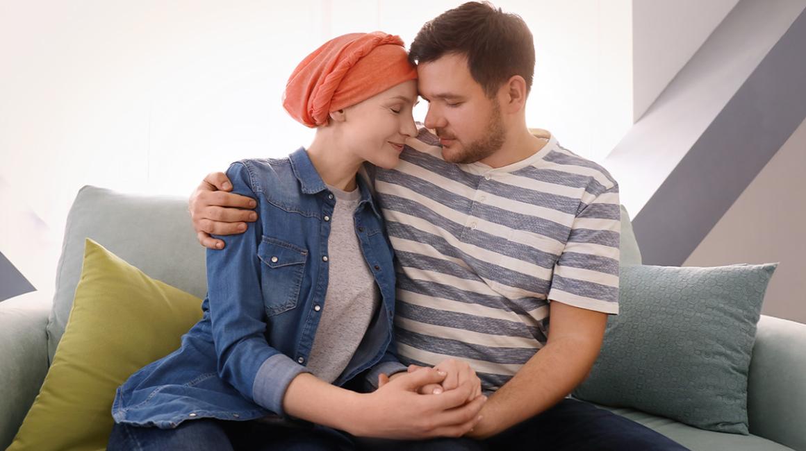 Młody mężczyzna i kobieta z chustką na głowie siedzą przytuleni na kanapie