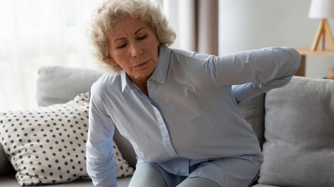 starsza pani z trudem siada na kanapie