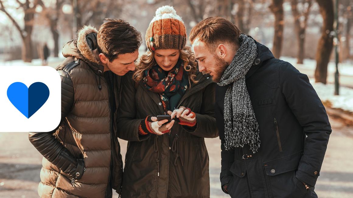 trzy osoby patrza w komorke trzymaną przez osobe w śrdoku