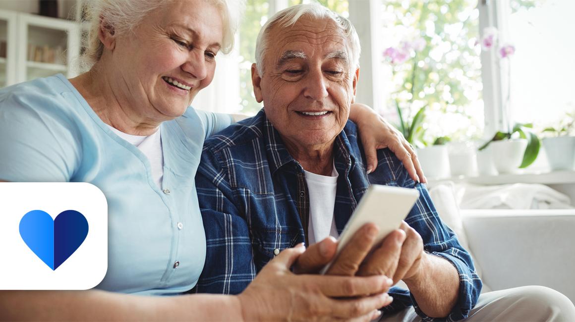 Starsza para na kanapie, żona pokazuje coś męzowi na komórce