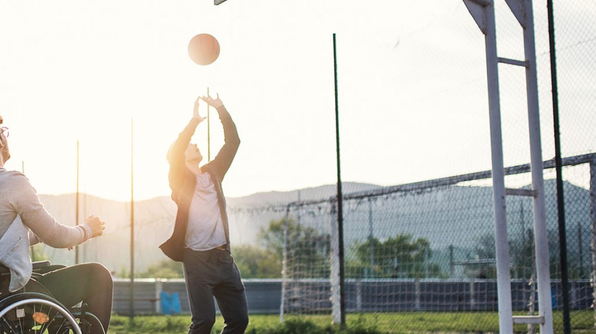 młodzi mężczyźni grają w koszykówkę, jeden jest na wózku