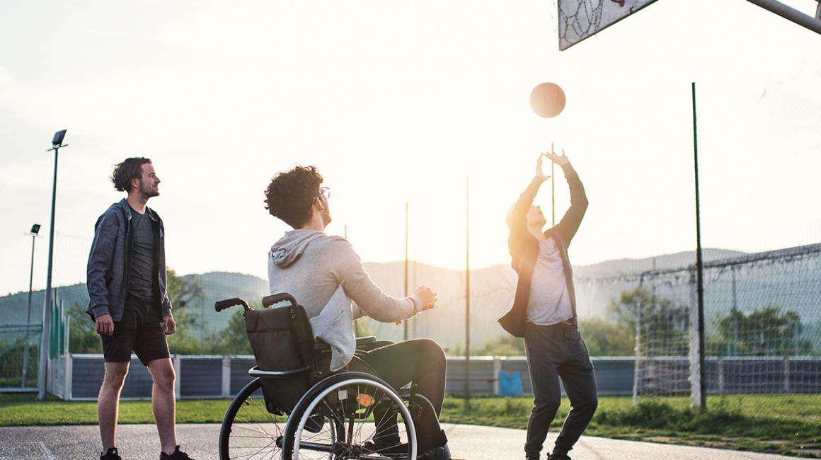 młodzi mężczyźni grają w koszykówkę, jeden jest na wózku