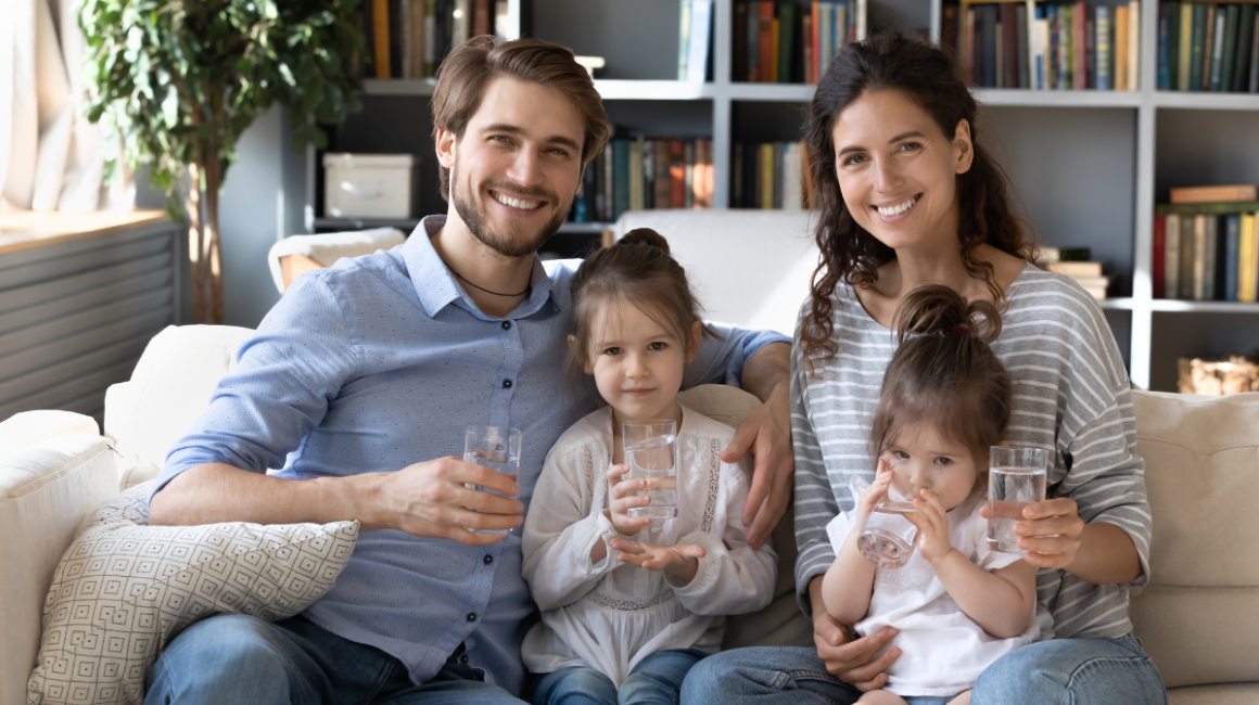 Rodzina siedzi na kanapie i trzyma wodę w szklankach