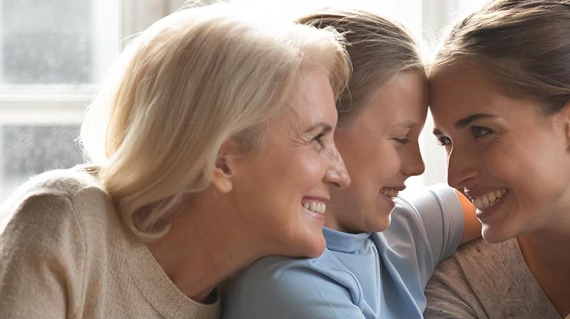 Babcia, mama i córka obejmują się i uśmiechają się do siebie.