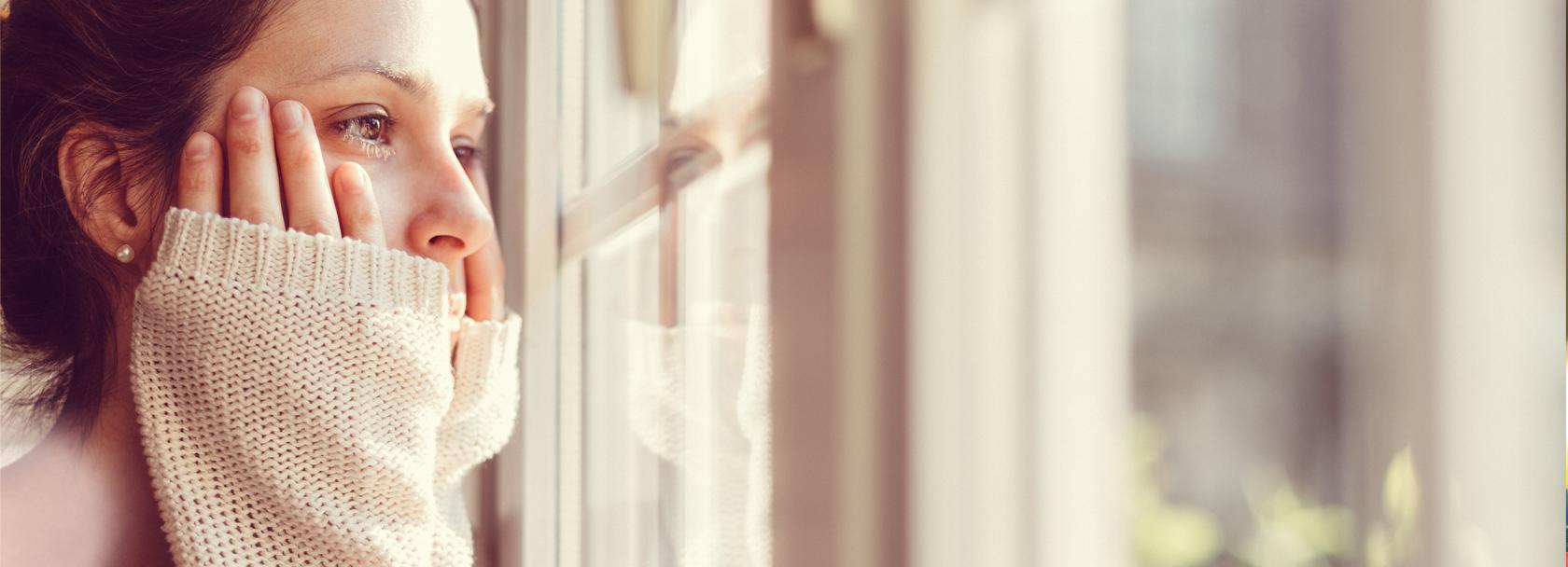 Kobieta obejmuje rękami policzki i patrzy za okno