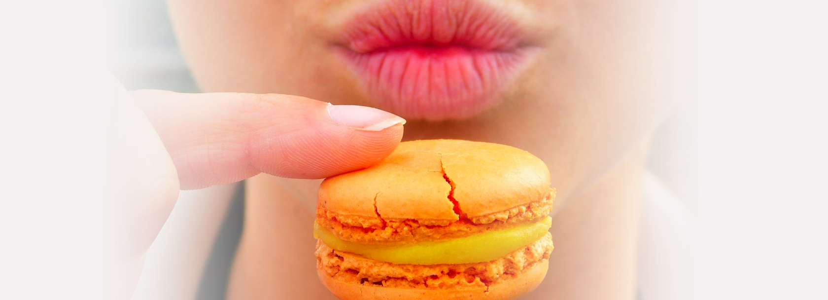 Widok dolnej części twarzy i ciasta przed nią trzymanego dwoma pacami prawej ręki. Ciastko z nadzieniem w środku.