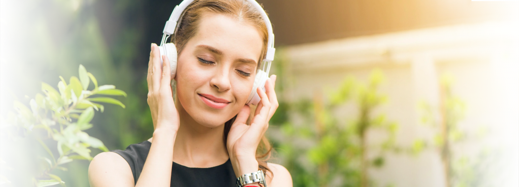 Uśmiechnięta dziewczyna z słuchawkami na uszach, na tle zieleni.