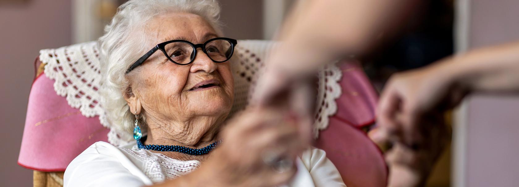 Starsza pani, której ktoś pomaga usiąść na łóżku