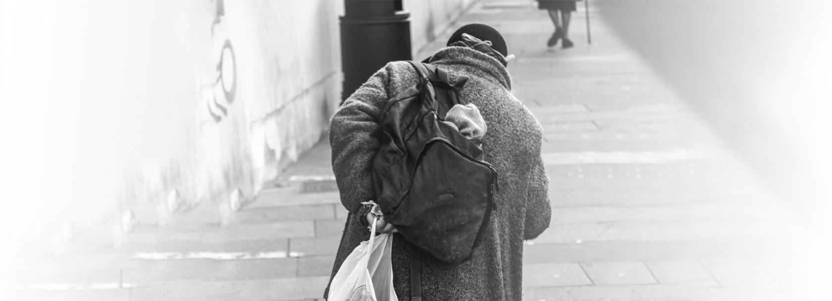 Bezdomna osoba z plecakiem i reklamówką, od tyłu, wchodząca po schodach