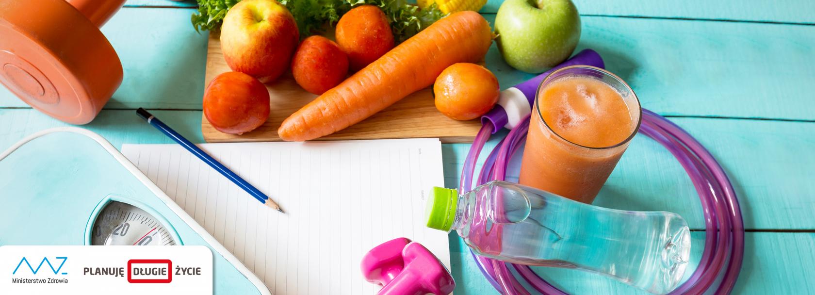 Leżące na deskach warzywa i owoce, waga, ciężarki, skakanka, szklanka z sokiem, kartka papieru