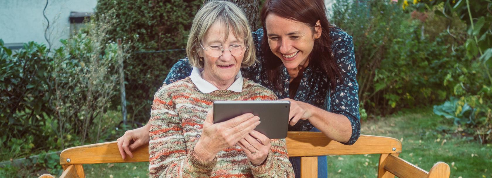 Dziewczyna pomaga zalogować się babci siedzącej na ławce w wiejskim ogródku