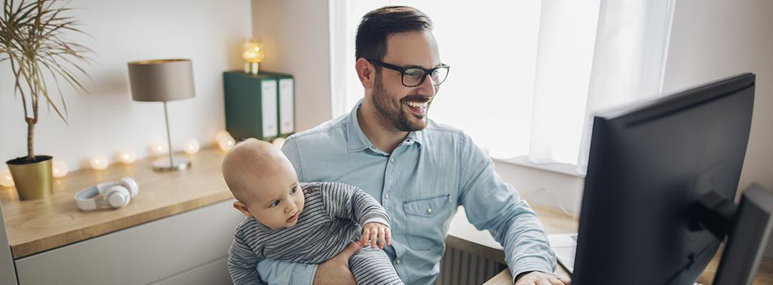 Tata z niemowlęciem na ręku przed komputerem
